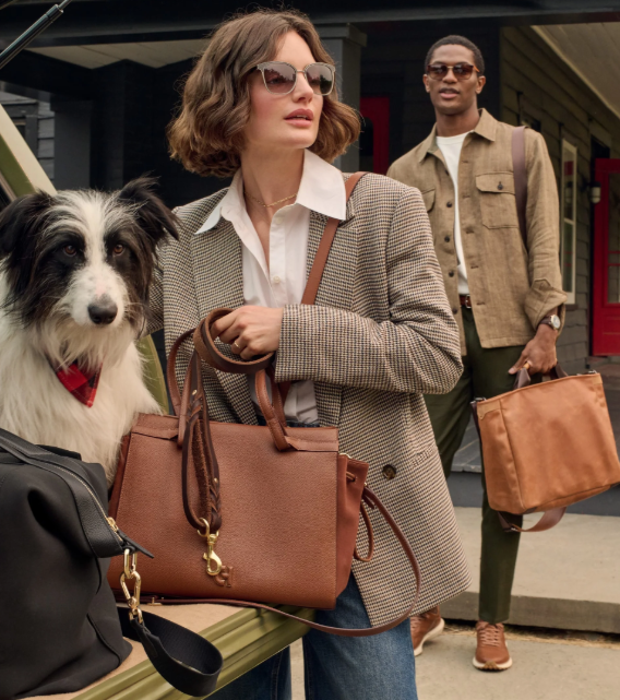 A lady model with suit holding a brown Cole tote bag and behind her a man with jacket holding another tote bag