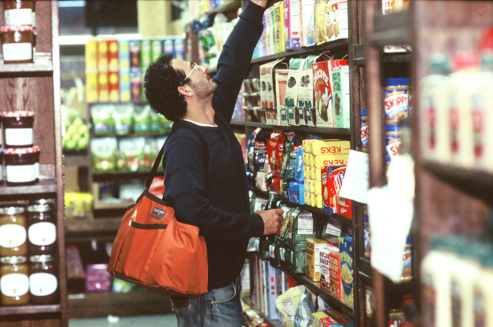 A man standing in a grocery store holding his orange Tom Bihn Truck Tote bag